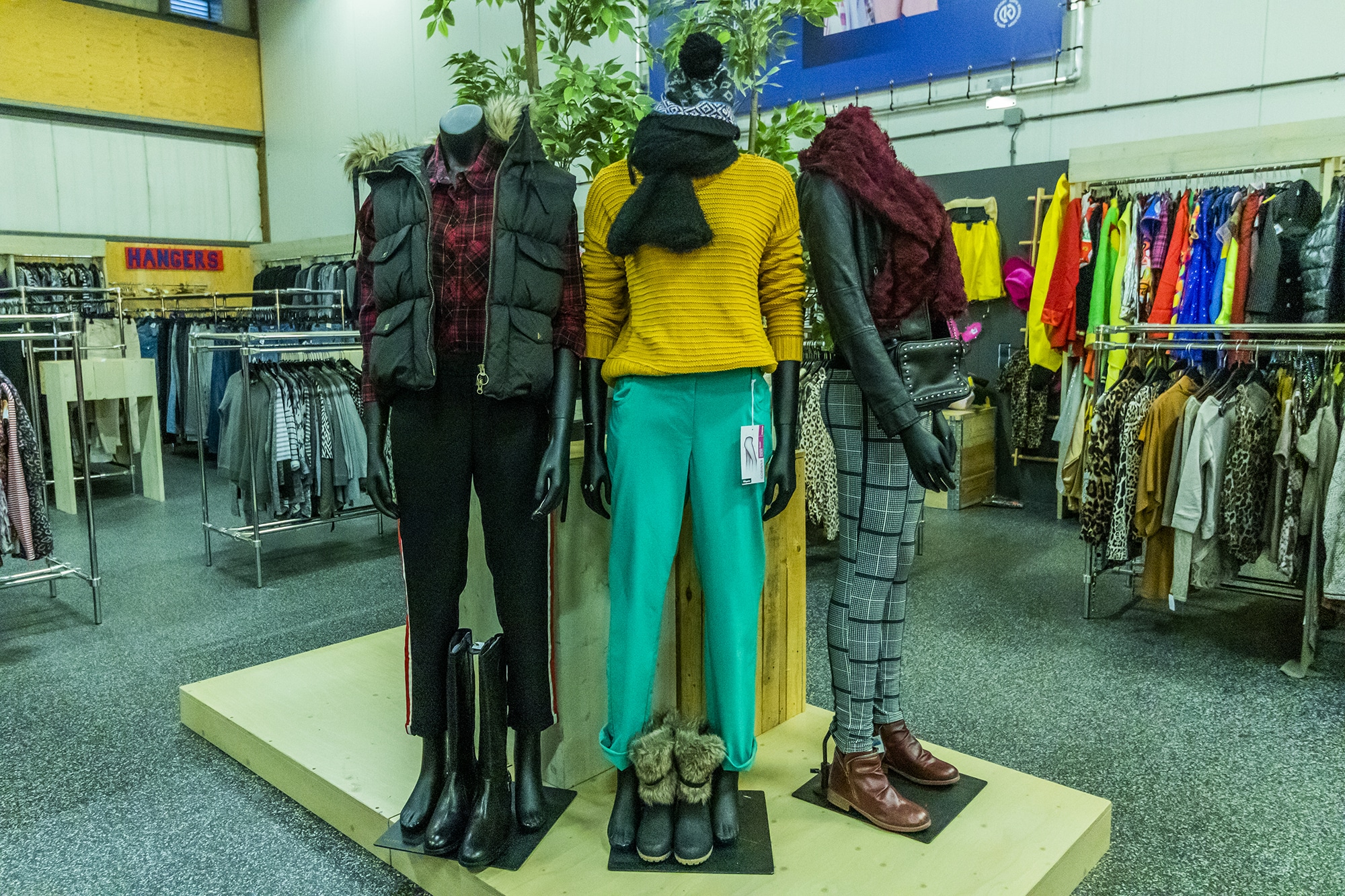 Op de foto zie je op de voorgrond 3 paspoppen staan. De paspoppen dragen winterkleding. Op de achtergrond zie je verschillende kledingrekken met winterkleding.