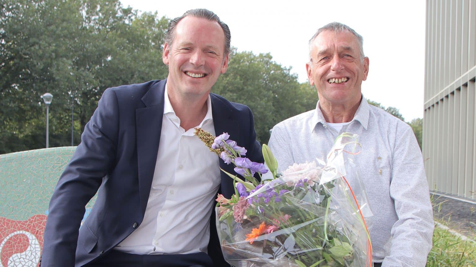 Op de foto staan Sjoerd van het Erve (directeur van Weener XL, links op de foto) en Ad van Erp (rechts op de foto). Ad van Erp houdt een bos bloemen vast.